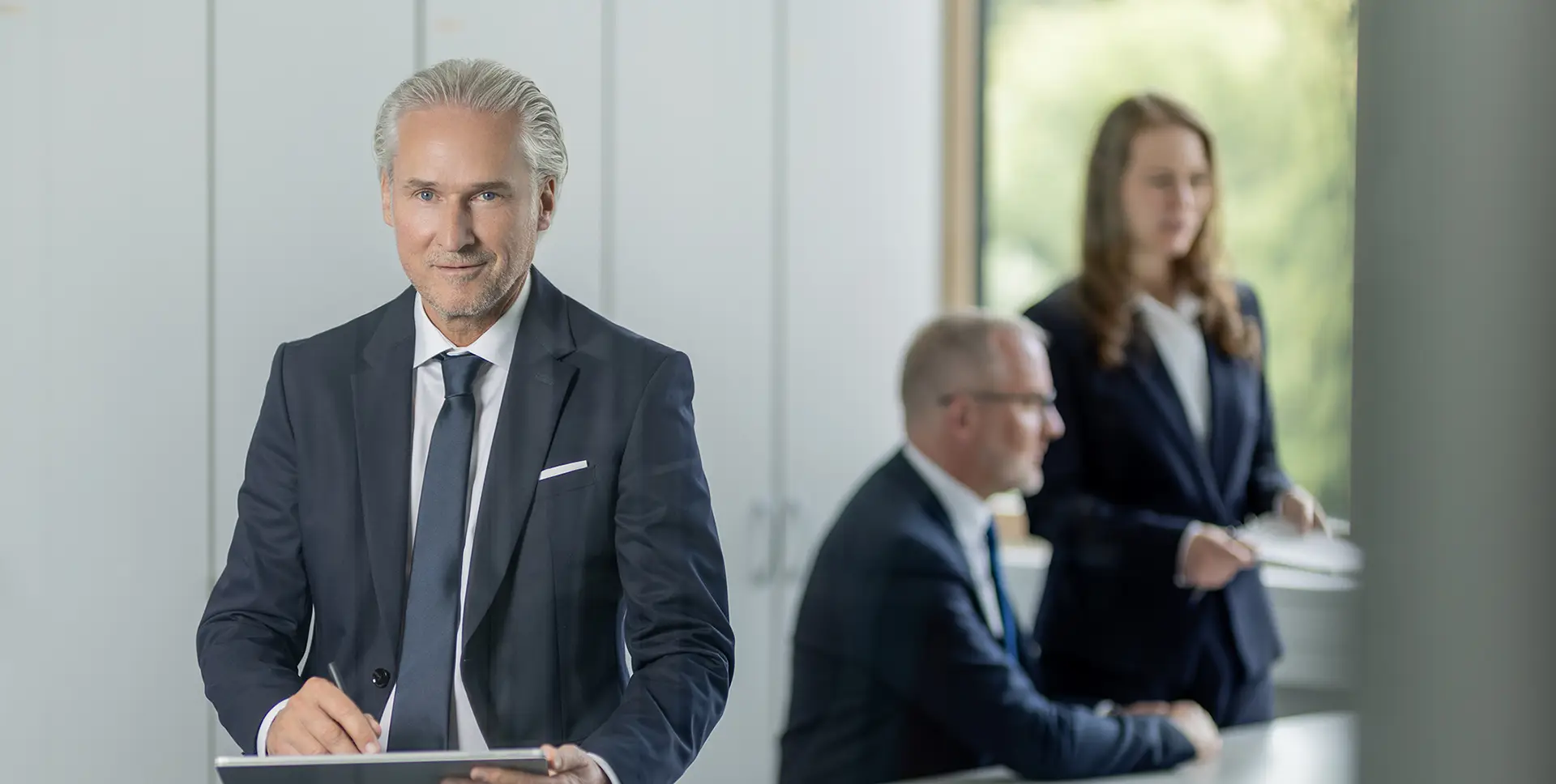 Herr Friedenauer im Büro mit Mitarbeitern im Hintergrund